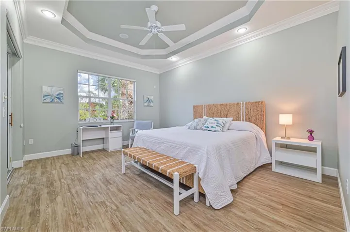 Bedroom featuring light wood finished floors, crown molding, a ceiling fan, and a raised ceiling