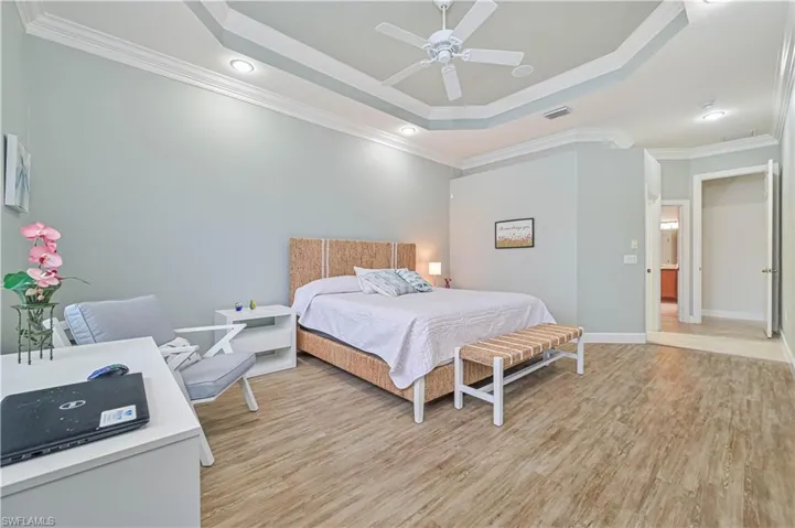 Bedroom with light wood-type flooring, crown molding, ceiling fan, a raised ceiling, and recessed lighting