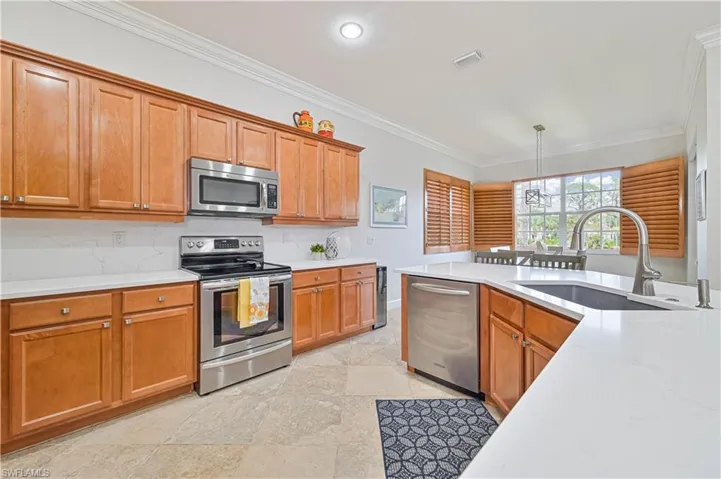Kitchen featuring stainless steel appliances, wood finish cabinetry, crown molding, pendant lighting, and light stone countertops