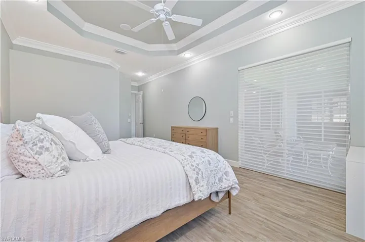 Bedroom with light wood-type flooring, access to exterior, crown molding, a ceiling fan, and a tray ceiling