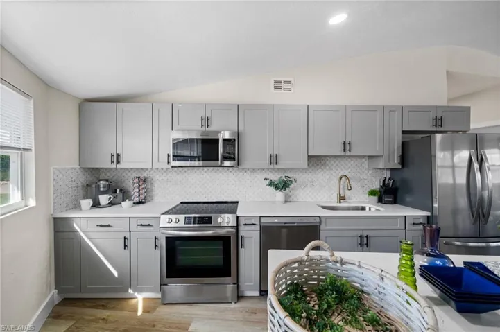 Kitchen with lofted ceiling, stainless steel appliances, gray cabinetry, light wood-style flooring, and light stone countertops