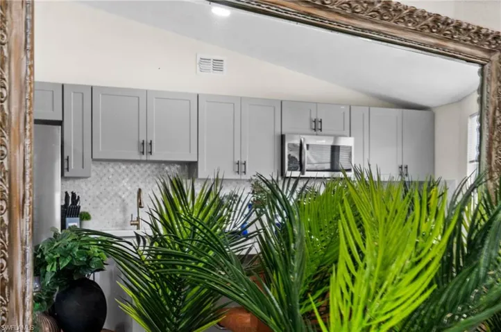 Kitchen with gray cabinetry, lofted ceiling, stainless steel microwave, and decorative backsplash