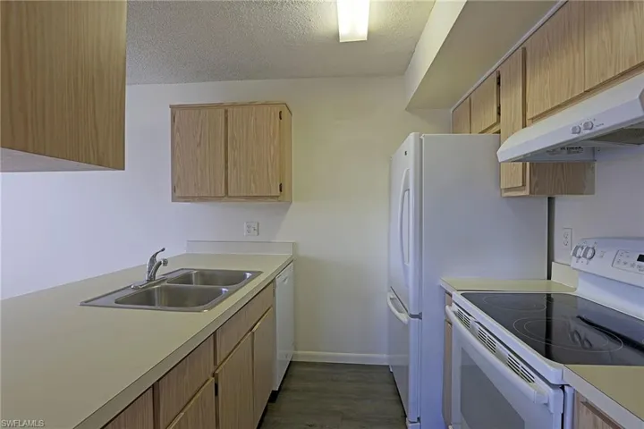 Kitchen with white appliances, a textured ceiling, under cabinet range hood, light countertops, and dark wood finished floors
