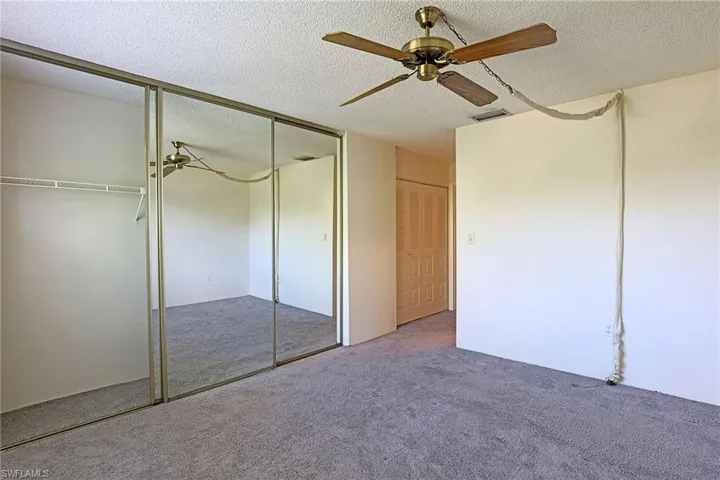 Unfurnished bedroom with a textured ceiling, a ceiling fan, a closet, and carpet flooring