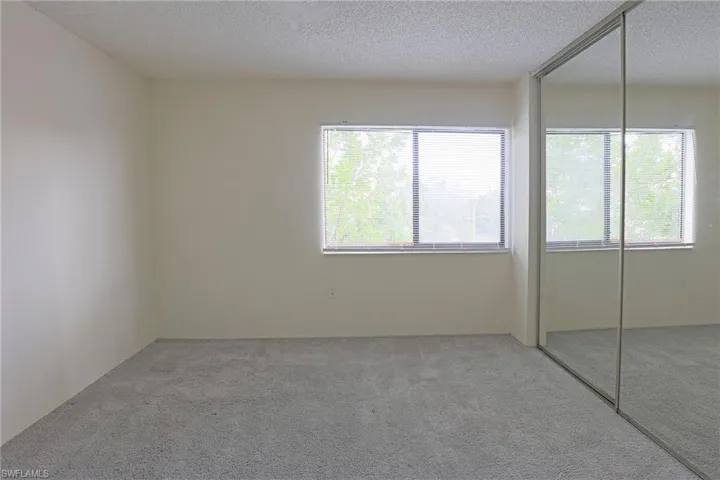 Unfurnished bedroom featuring a textured ceiling, a closet, multiple windows, and carpet floors