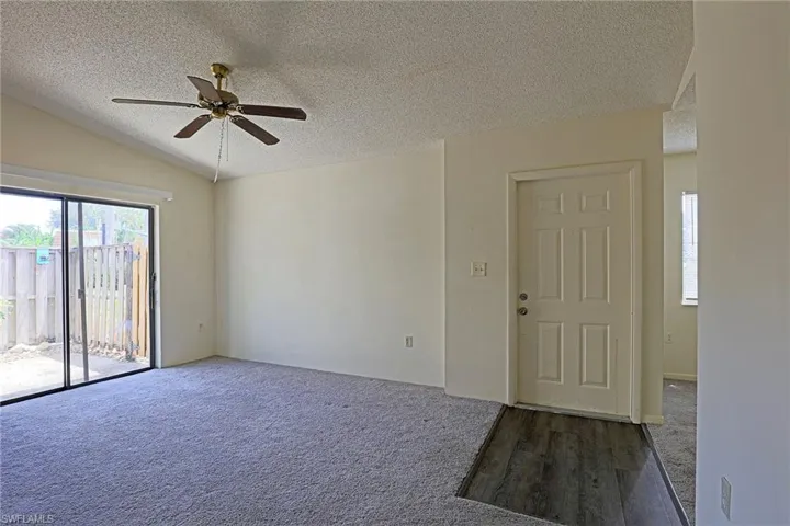 Carpeted empty room featuring a textured ceiling, ceiling fan, and vaulted ceiling
