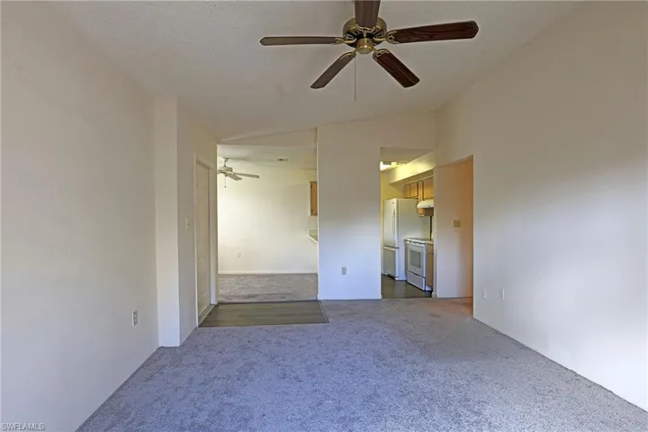 Spare room featuring lofted ceiling, dark colored carpet, ceiling fan, and a textured ceiling