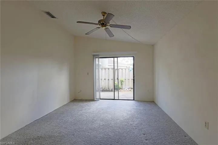 Carpeted empty room featuring vaulted ceiling, a textured ceiling, and ceiling fan