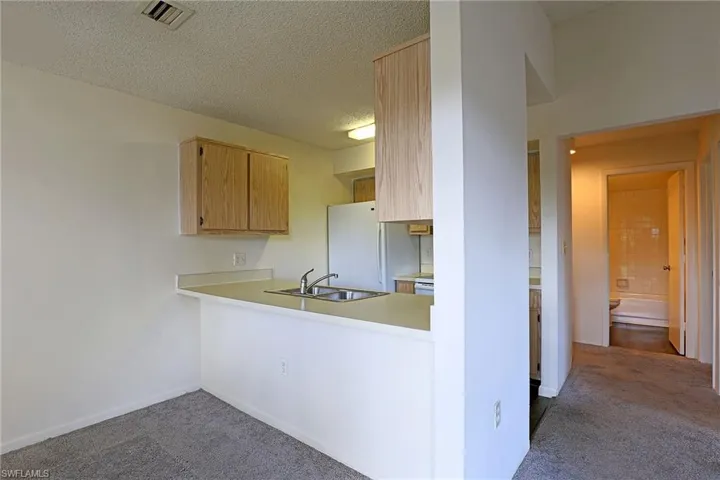 Kitchen featuring light countertops, freestanding refrigerator, dark carpet, a textured ceiling, and a peninsula