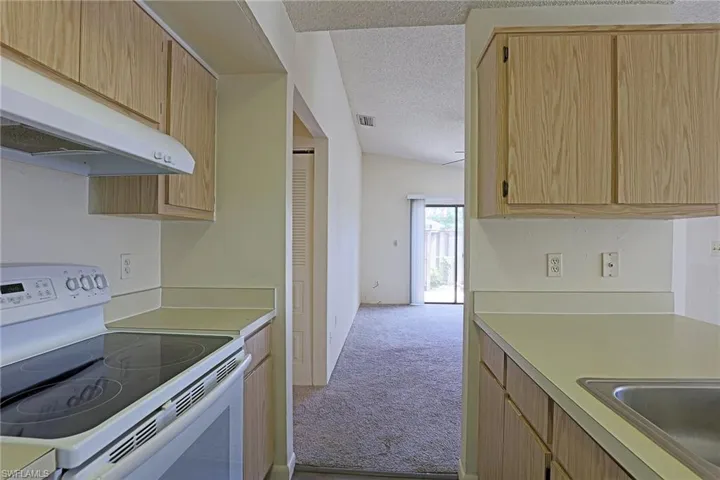 Kitchen with white range with electric stovetop, light countertops, under cabinet range hood, light carpet, and a textured ceiling