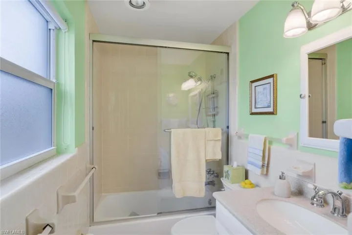 Full bathroom featuring bath / shower combo with glass door, tile walls, backsplash, vanity, and toilet