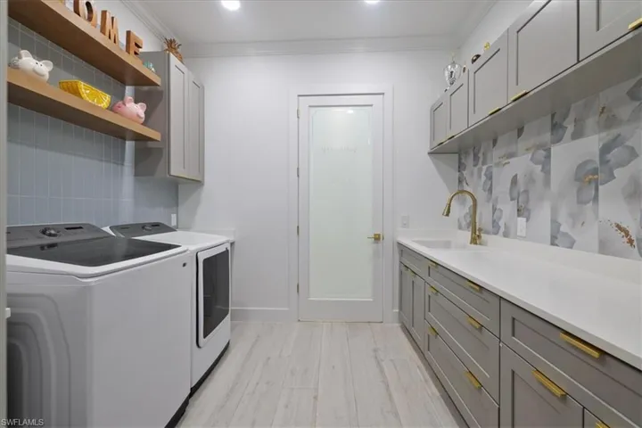 Laundry room featuring ornamental molding, light wood-type flooring, washer and clothes dryer, and cabinet space