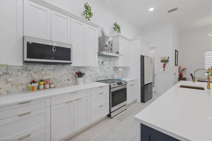 Kitchen featuring appliances with stainless steel finishes, white cabinets, wall chimney exhaust hood, ornamental molding, and backsplash