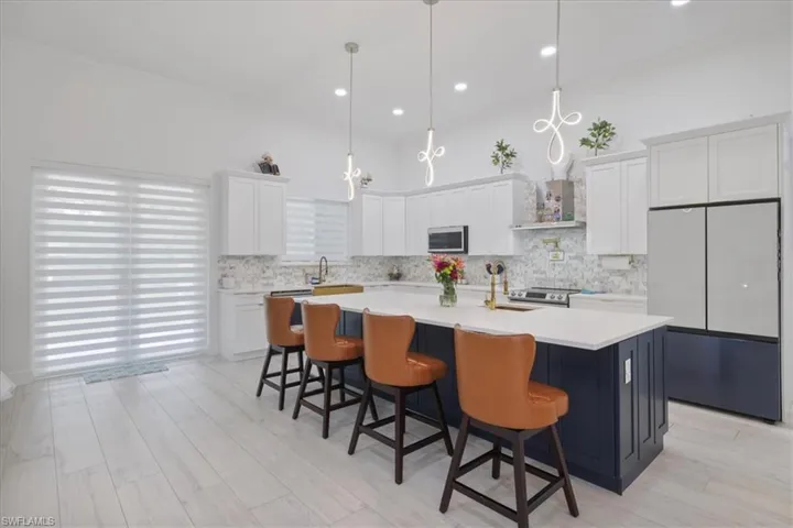 Kitchen featuring white cabinets, appliances with stainless steel finishes, crown molding, backsplash, and a kitchen island with sink