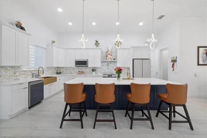 Kitchen with ornamental molding, white cabinetry, backsplash, hanging light fixtures, and a kitchen island with sink