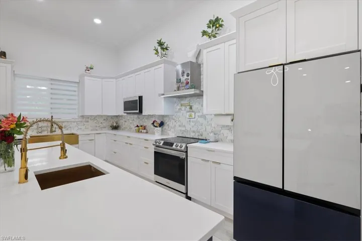 Kitchen with stainless steel appliances, white cabinets, ornamental molding, wall chimney exhaust hood, and tasteful backsplash