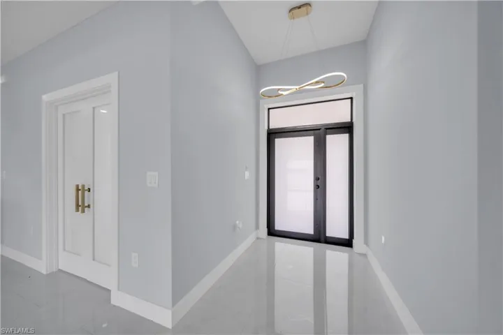 Entryway featuring a modern double-door entry with transom window, contemporary chandelier, high ceilings, and polished tile flooring