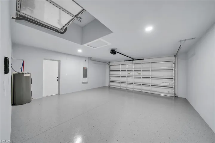 Spacious garage featuring a durable epoxy floor, bright recessed lighting, overhead garage door opener, and a side-entry door