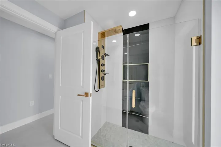 Modern shower enclosure featuring clear glass panels, gold-toned hardware, and a multi-function shower system