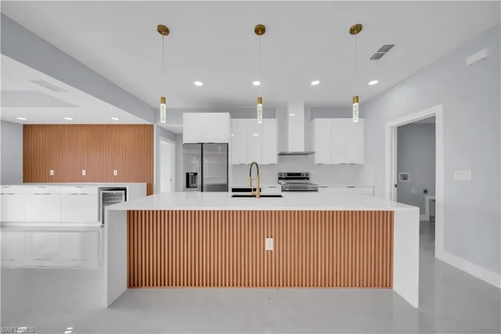 Modern kitchen featuring a waterfall island with wood slat detailing, gold-tone pendant lighting, and stainless steel appliances