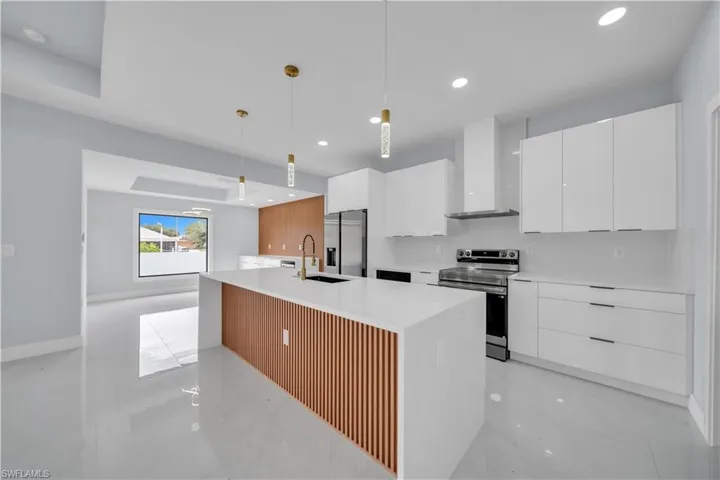 Modern kitchen featuring a waterfall island with slatted wood-finish paneling, white shaker cabinetry, stainless steel appliances, recessed lighting, and light-toned flooring