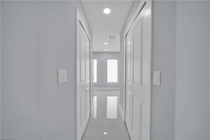 Bright interior corridor featuring recessed lighting, white paneled doors, light grey wall paint, white baseboards, and reflective tile flooring