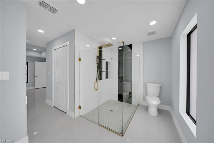 Spacious bathroom featuring a glass-enclosed shower with gold-finish fixtures, white tile surround, and a mosaic floor