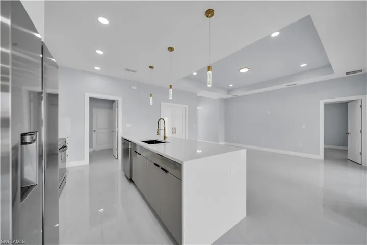 Contemporary kitchen featuring a large island with a white countertop and undermount sink, stainless steel appliances, recessed lighting, and elegant pendant fixtures