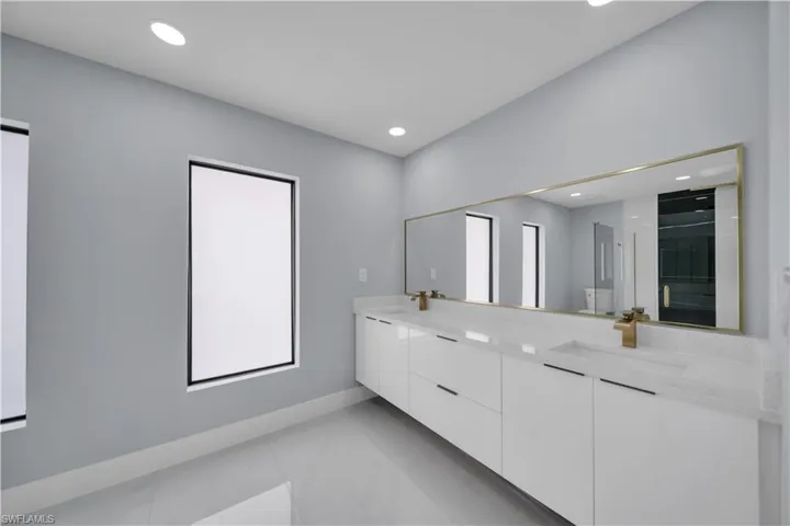 Spacious bathroom featuring a dual vanity with white cabinetry, light-toned countertops, and gold-finish fixtures