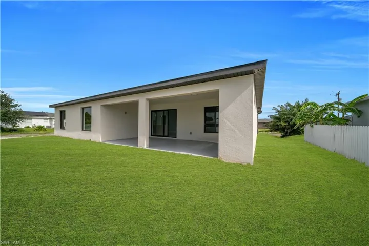 Expansive rear yard featuring a covered patio with concrete flooring, stucco exterior, and black-framed sliding glass doors
