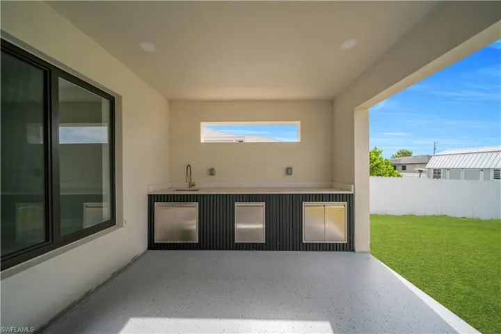 Covered patio featuring an outdoor kitchen with countertop space, an undermount sink with a brass-finish faucet, stainless steel cabinetry, and a horizontal transom window