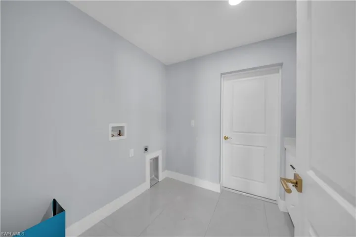Laundry room featuring light gray walls, white baseboards, and a white two-panel door with a brass-finish doorknob
