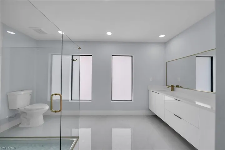 Spacious bathroom featuring a frameless glass shower enclosure, a white toilet, and two rectangular windows with black frames