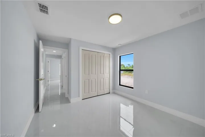 Light-filled room featuring white tile flooring, a large window, bi-fold closet doors, and recessed lighting in the hallway