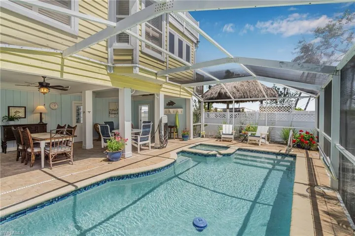 View of swimming pool with glass enclosure, a patio area, a pool with connected hot tub, outdoor dining area, and a sunroom