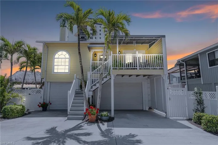 Raised beach house with a gate, concrete driveway, a garage, and stairs