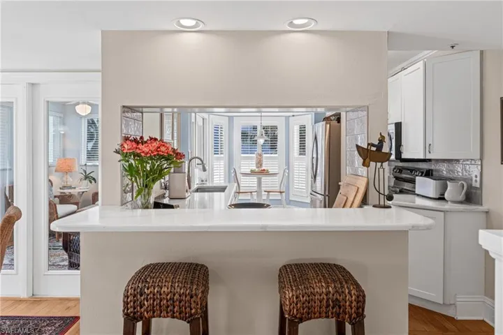 Kitchen featuring white cabinetry, freestanding refrigerator, a breakfast bar, light wood finished floors, and tasteful backsplash