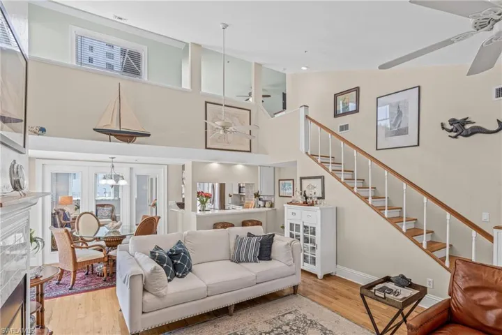 Living room with ceiling fan, light wood-style flooring, a high ceiling, stairway, and a chandelier