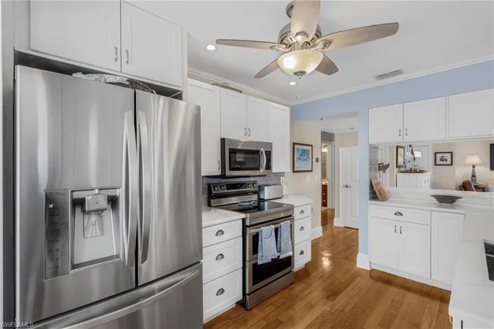 Kitchen with stainless steel appliances, crown molding, white cabinets, light wood-style flooring, and ceiling fan