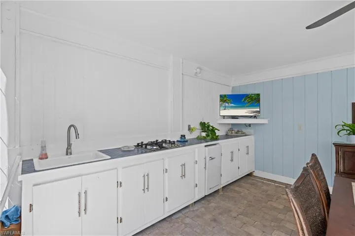Kitchen featuring white cabinets, stainless steel gas cooktop, ornamental molding, ceiling fan, and wood walls