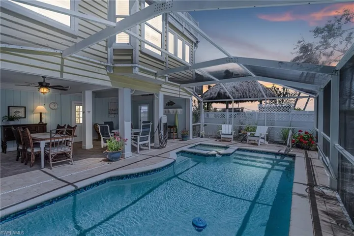 Pool at dusk featuring a patio area, glass enclosure, a sunroom, a pool with connected hot tub, and outdoor dining area
