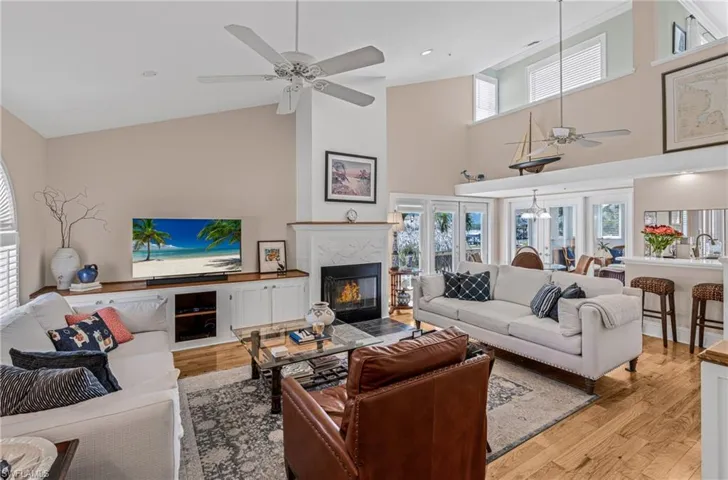 Living room featuring healthy amount of natural light, light wood finished floors, a high end fireplace, high vaulted ceiling, and ceiling fan