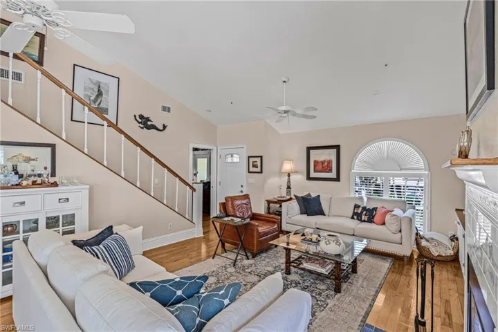 Living area with a ceiling fan, stairway, a fireplace, wood finished floors, and high vaulted ceiling