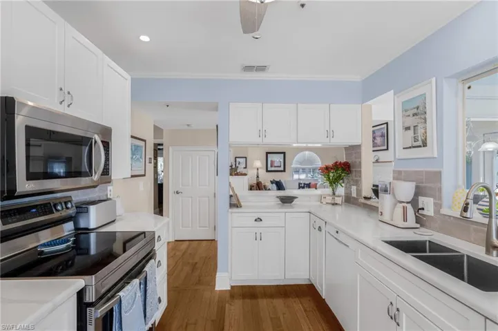 Kitchen featuring appliances with stainless steel finishes, white cabinetry, dark wood-style floors, ceiling fan, and light stone countertops