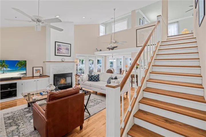 Living room with high vaulted ceiling, a high end fireplace, stairs, and light wood-type flooring