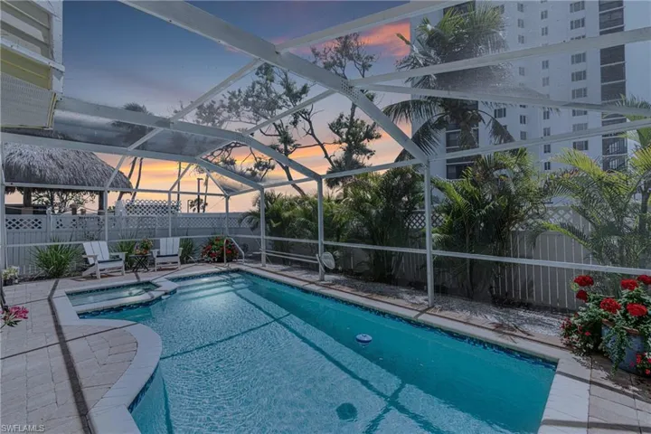 Pool at dusk with a fenced backyard, a lanai, and a pool with connected hot tub