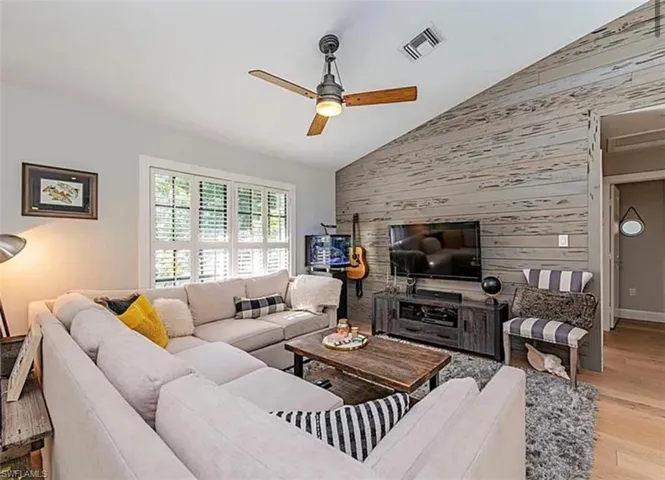 Living area featuring wood walls, light wood-style flooring, a ceiling fan, vaulted ceiling, and an accent wall