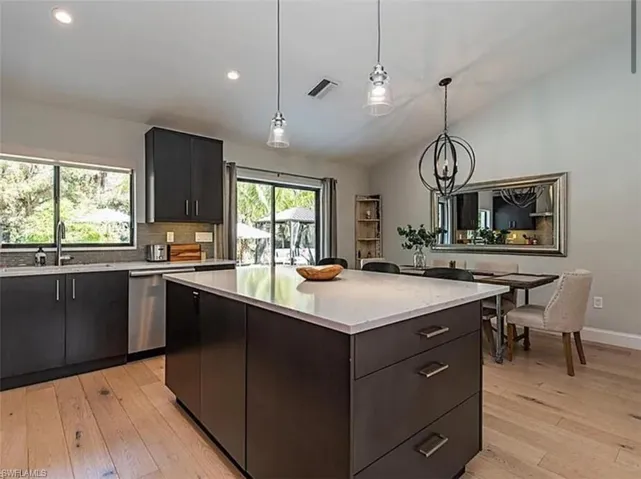 Kitchen with dark cabinetry, light wood finished floors, dishwasher, a kitchen island, and lofted ceiling