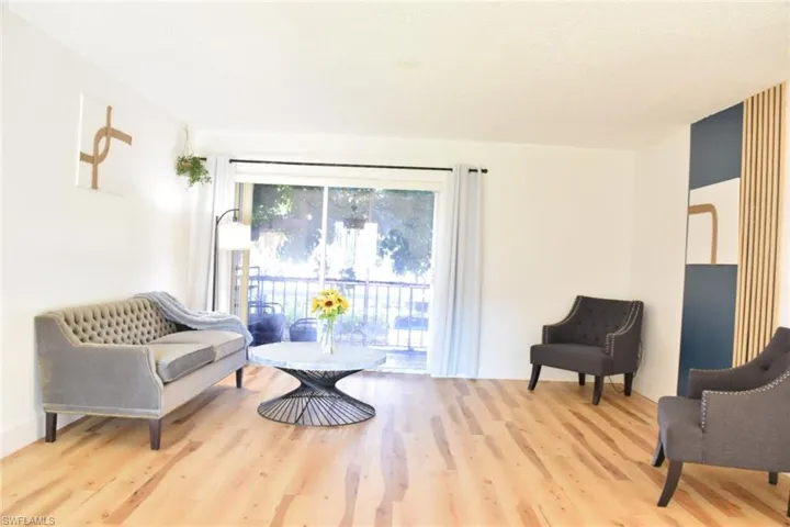 Bright living space featuring light wood-finish flooring, white walls, and a sliding glass door leading to a balcony