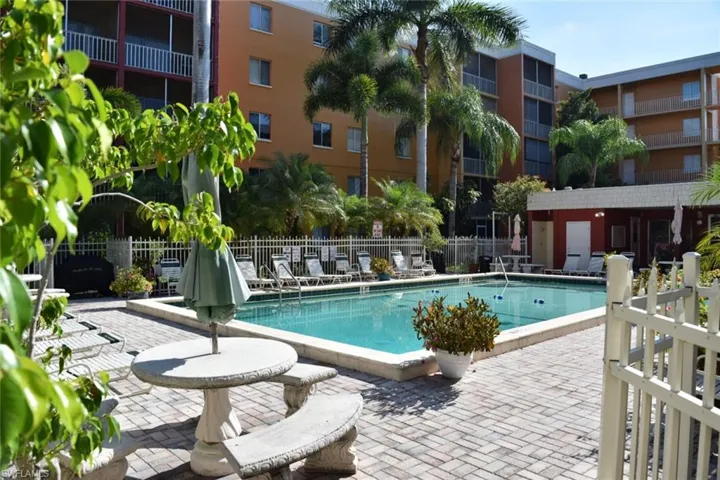 Swimming pool with a paved patio surround, featuring multiple lounge chairs and a white picket fence